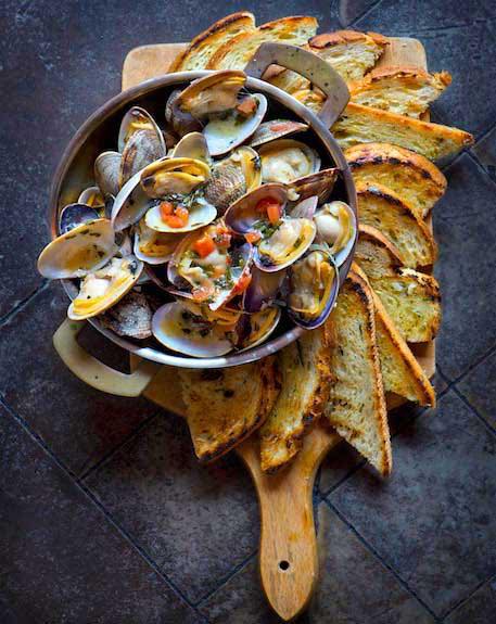 Bowl of mussels on a cutting board holding toast