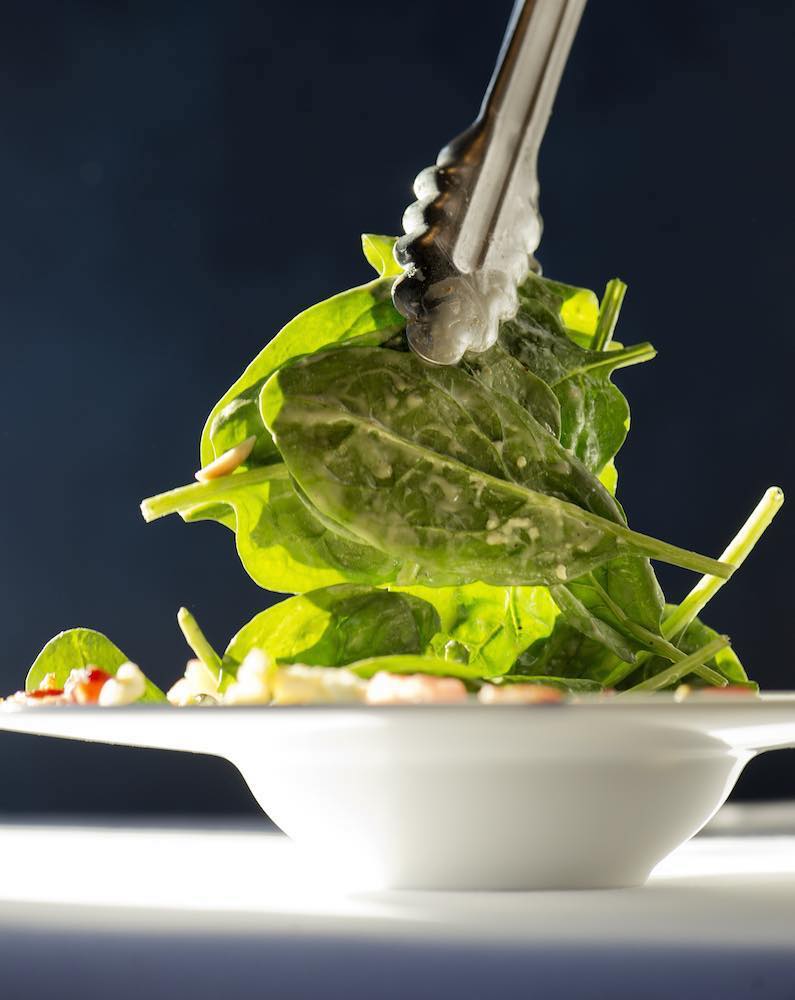Spinach salad leaves being lifted by tongs, back lit