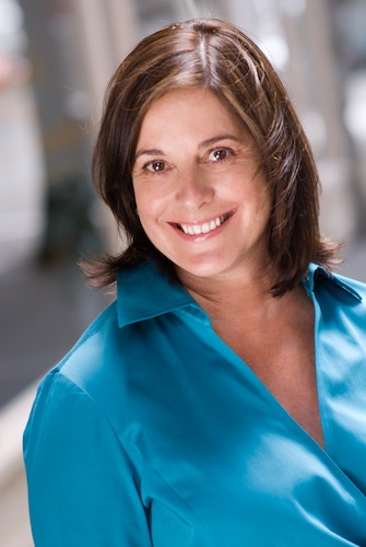 Shows a professional headshot of a business coach, woman, casual, half body, outside
