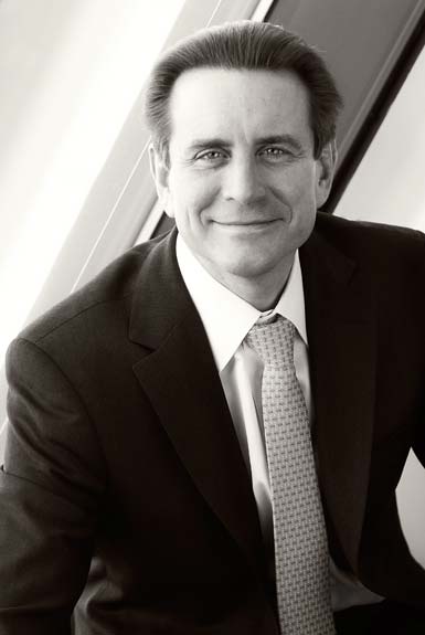 Shows a professional business headshot of a man, formal, suit, half body, ambient background