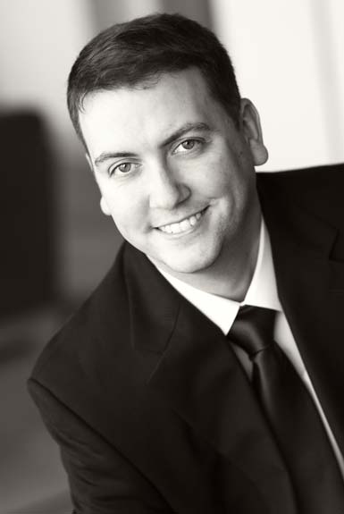 Shows a professional business headshot of a man, formal, suit, half body, ambient background
