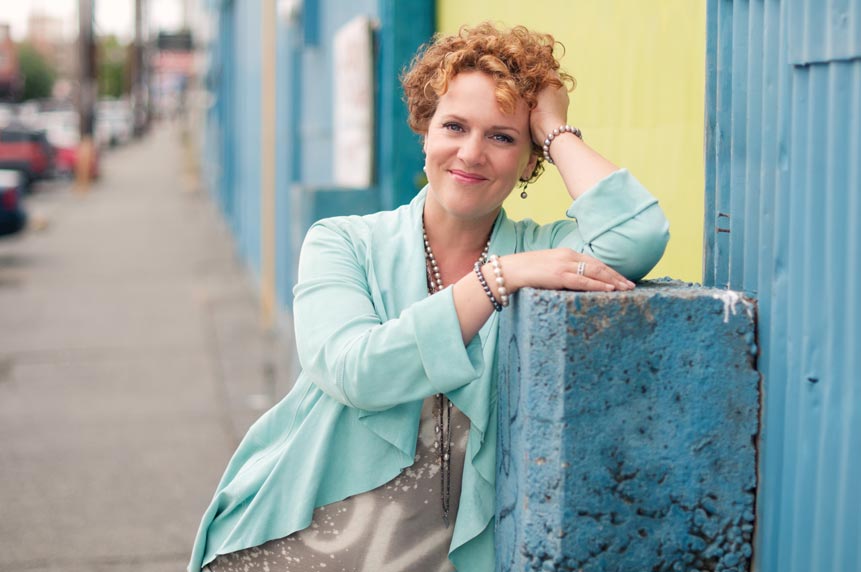Personal branding portrait of a woman in light blue outside leaning on concrete post