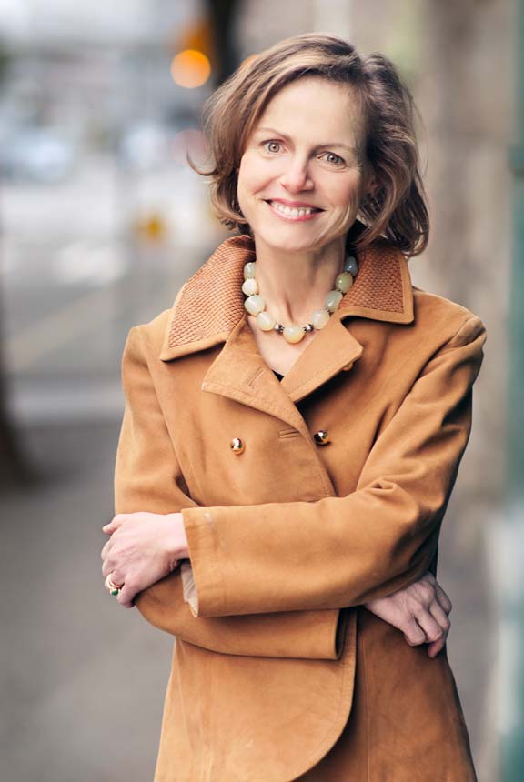 Shows a professional business headshot of a woman outside waering coat and smiling