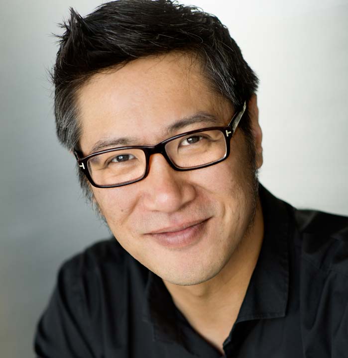 Shows a professional business headshot of a man in a black shirt wearing glasses