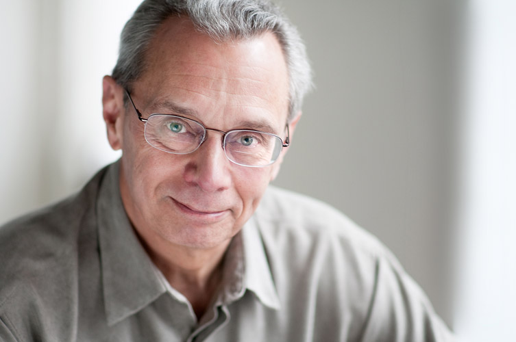 Shows a professional business headshot of a man wearing gray shirt and glasses