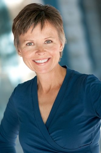 Shows a professional business headshot of a woman in blue top, short hair, smiling